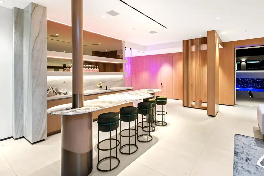 A bar with a stone counter, backlit shelving and a row of stools