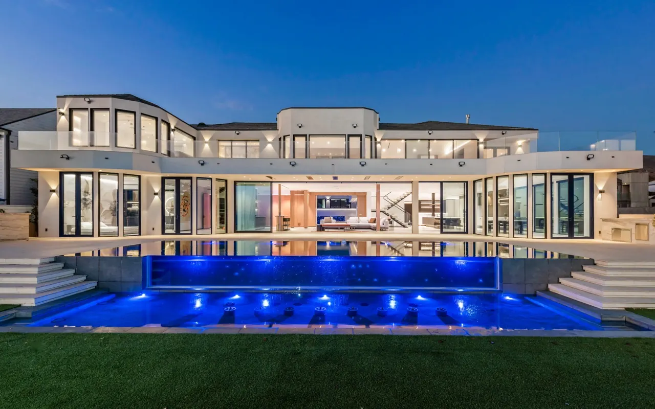 The ocean elevation at twilight: two floors of glass above a lit, glass-edged pool