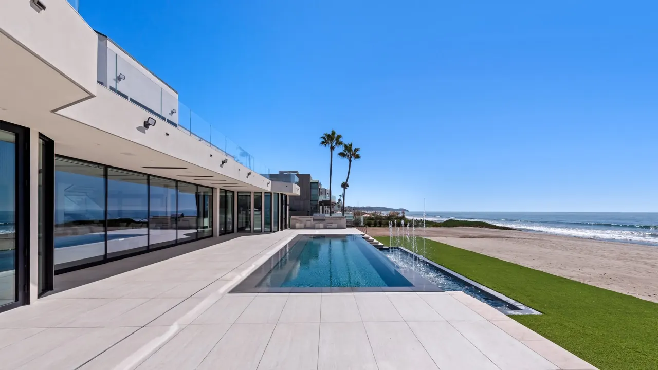 A lap pool running along the glazed ground floor toward the beach and palms