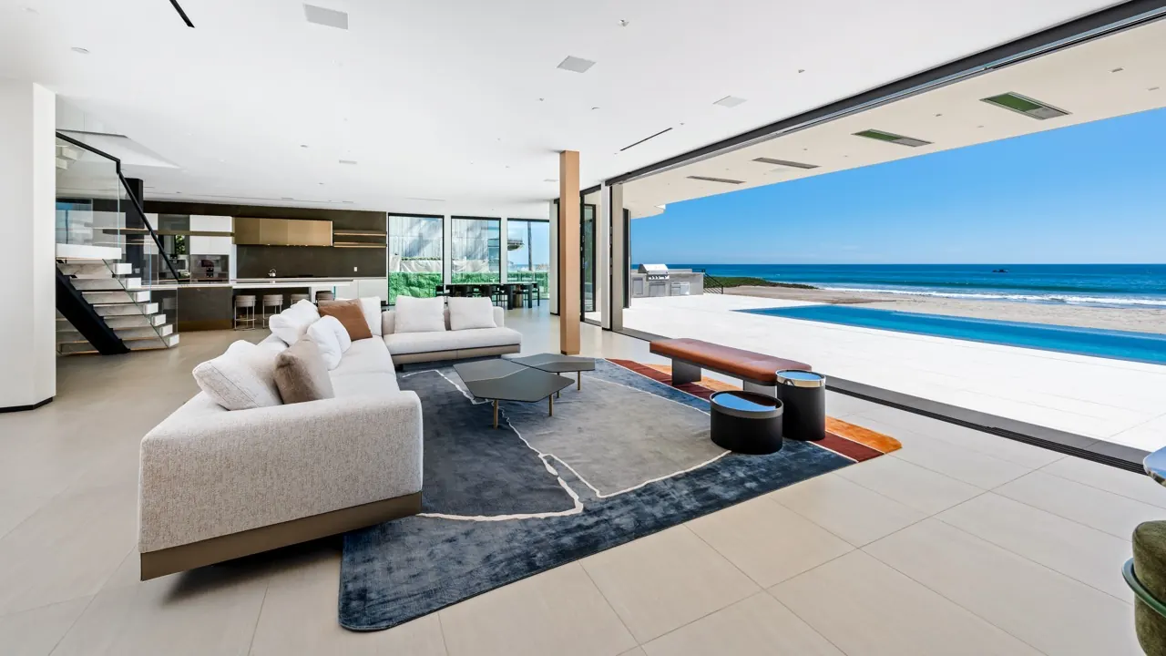 The living room with its glass wall slid fully open to the pool deck and ocean