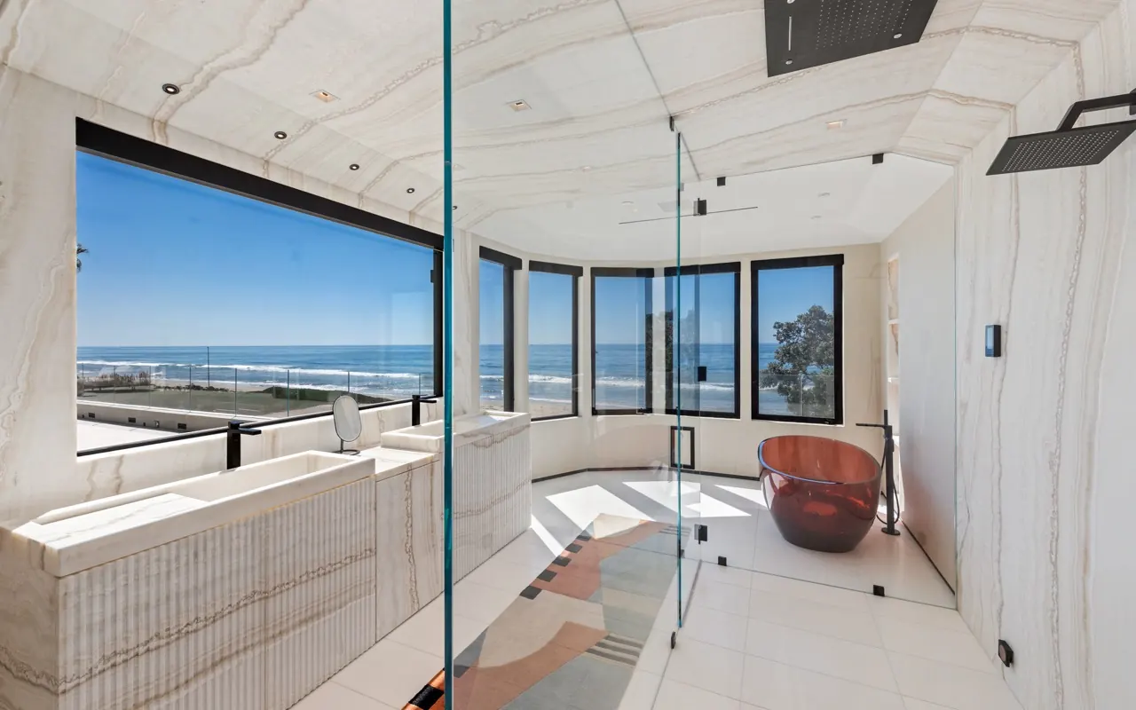 The primary bath: onyx-clad walls and a copper tub in a curved bay of windows over the beach