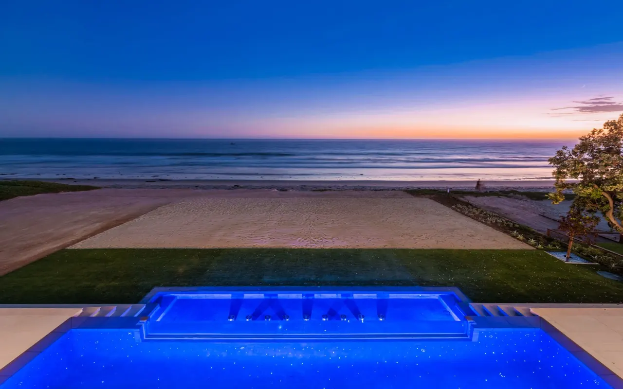 The pool and spa at dusk, lit blue, lined up with the horizon over the beach