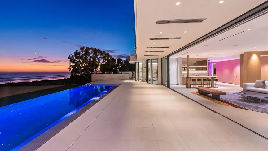 A lap pool running the length of a Malibu house at dusk with the ocean beyond