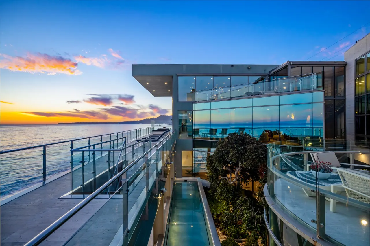 A long terrace and glass-floored water channel at sunset, with the coastline beyond