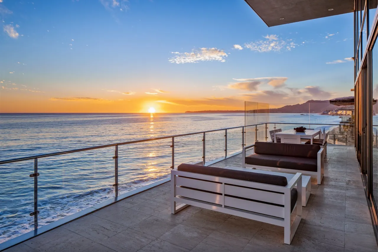 The ocean terrace at sunset, outdoor sofas along a glass balustrade