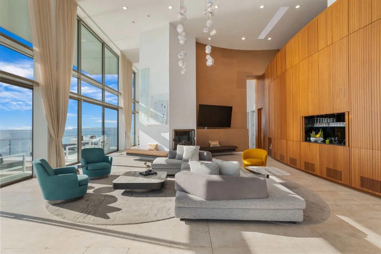 The double-height living room: a timber-panelled wall with fireplace and bar, and full-height glass to the ocean