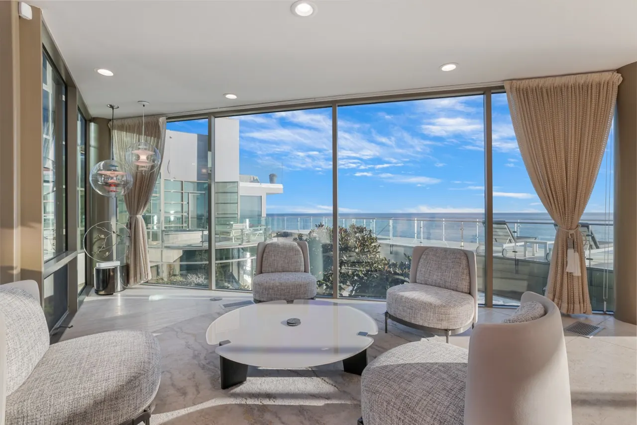A seating group of curved lounge chairs set against floor-to-ceiling ocean windows