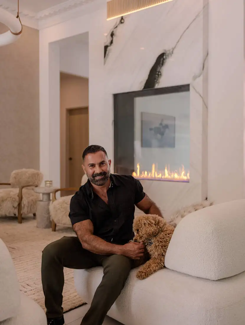Ali Rad seated in a completed living room at Shadybrook Drive, beside a marble fireplace wall