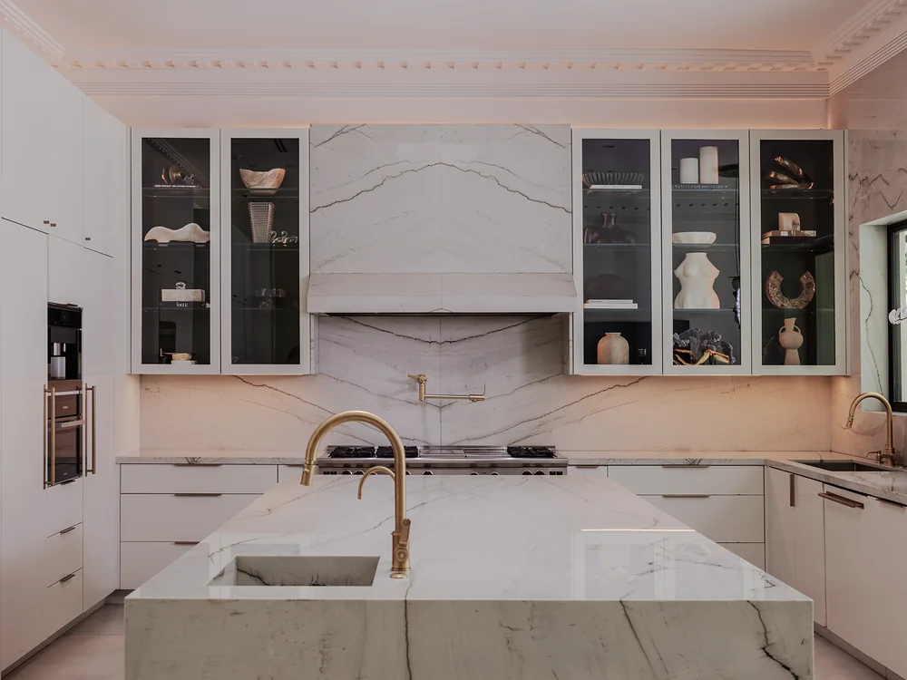 The kitchen: white stone hood, glass cabinets and a waterfall island