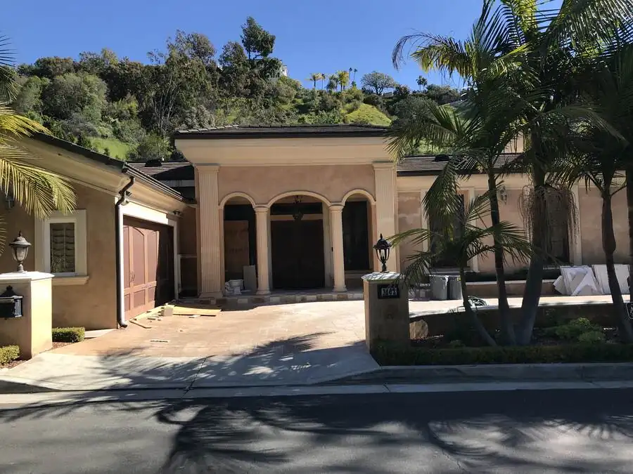 The house before work: beige stucco, a tiled hip roof over an arched portico with turned columns and balustrades