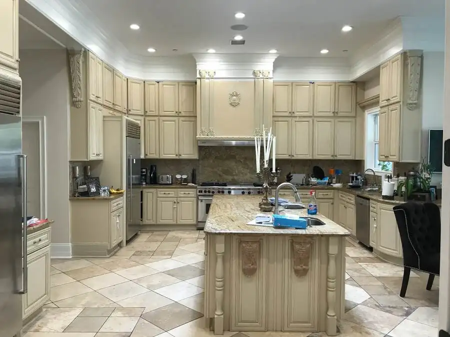 The kitchen before work: cream raised-panel cabinetry, granite counters and a tumbled-stone floor