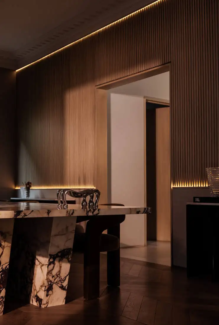 A dining room in dark timber with a figured stone table and concealed cove lighting