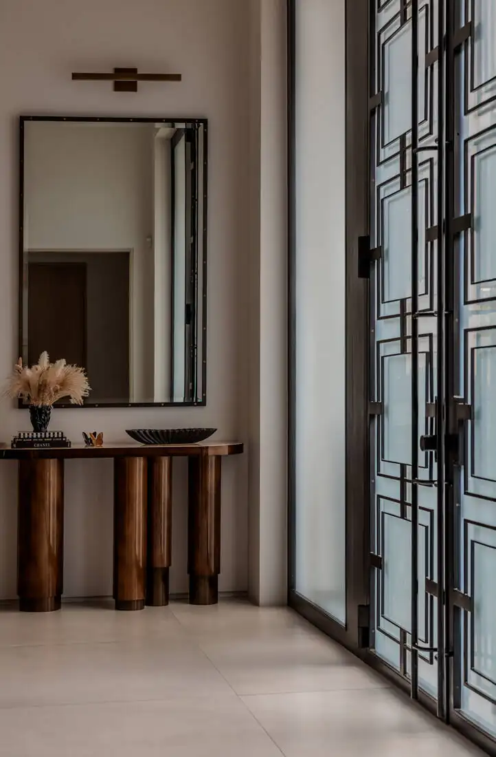 The entry after work: full-height black steel-and-glass doors with a timber console and a tall mirror