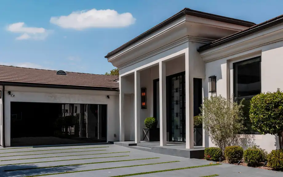 The remodelled front elevation of a Los Angeles house, a flat portico on square columns with black steel-and-glass doors