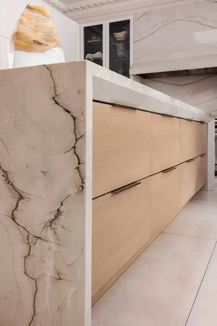 A close view of a marble island with a mitred waterfall edge meeting timber cabinetry
