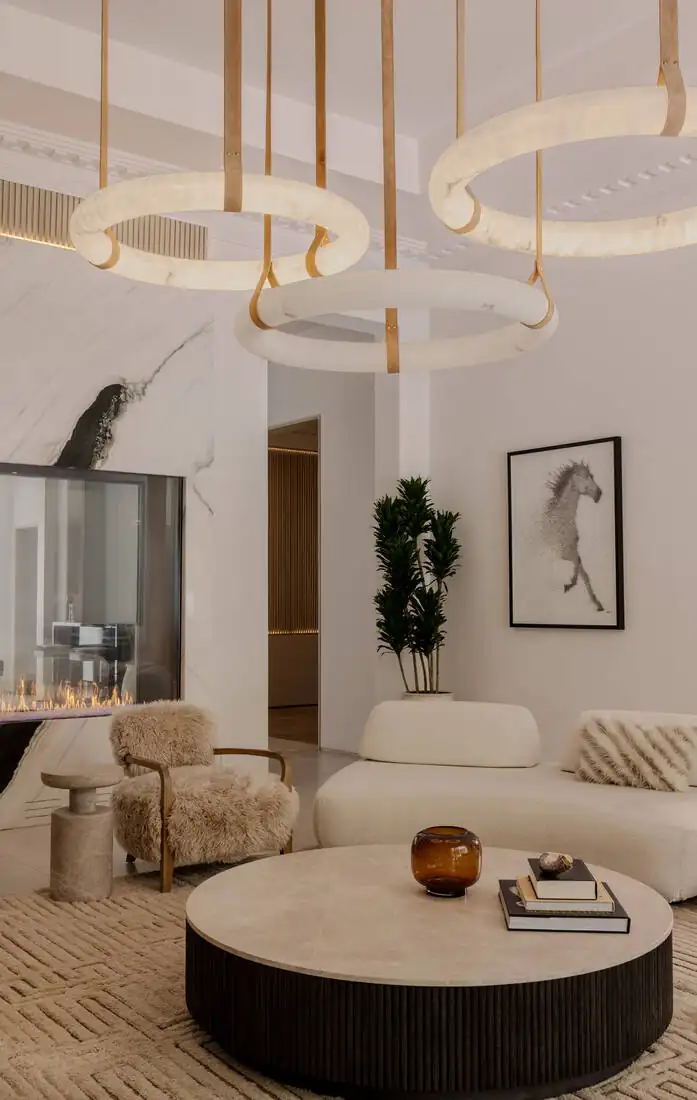 A living room with a brass ring chandelier, a round travertine table and low seating