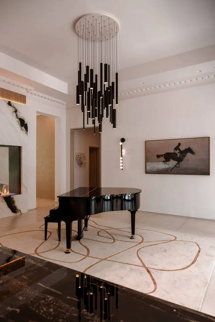 A tall reception room with a black linear chandelier, a grand piano and a marble slab wall