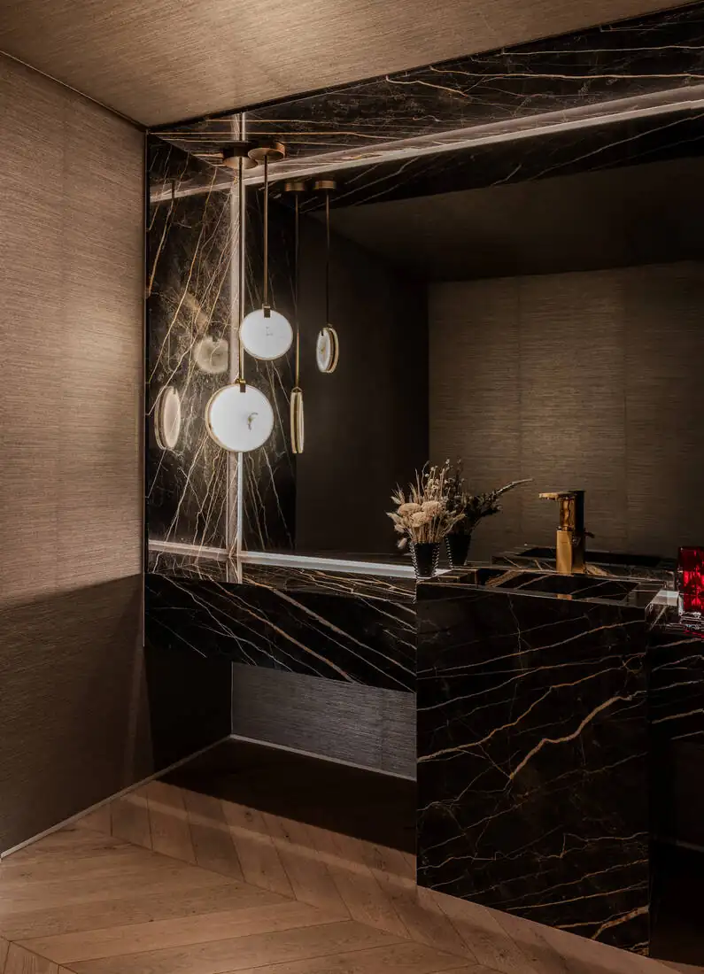 A powder room lined in black and gold marble with a floating stone basin and small pendant lights