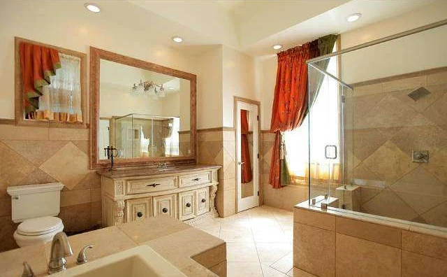 The primary bathroom before: framed mirror, carved vanity and travertine tile