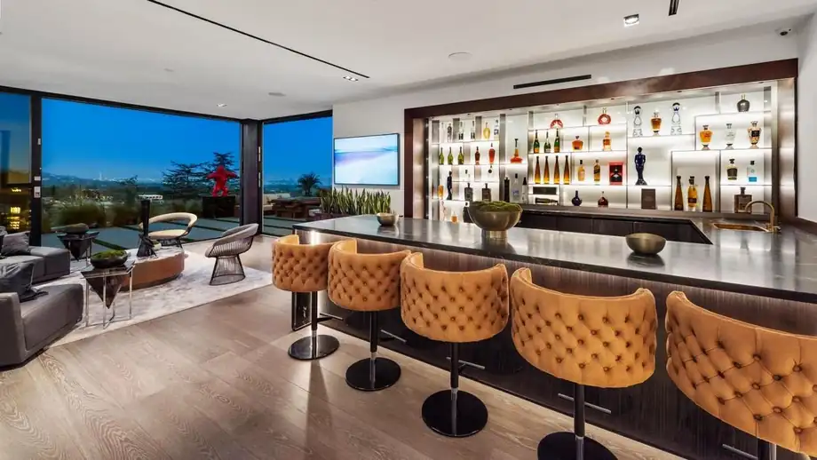 A bar with backlit shelving, a stone counter and stools