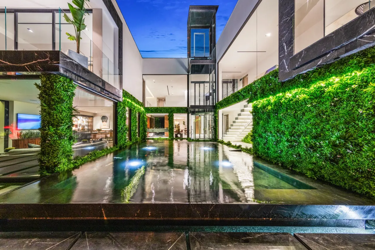 A central courtyard with a reflecting pool between planted green walls, a glass stair tower beyond