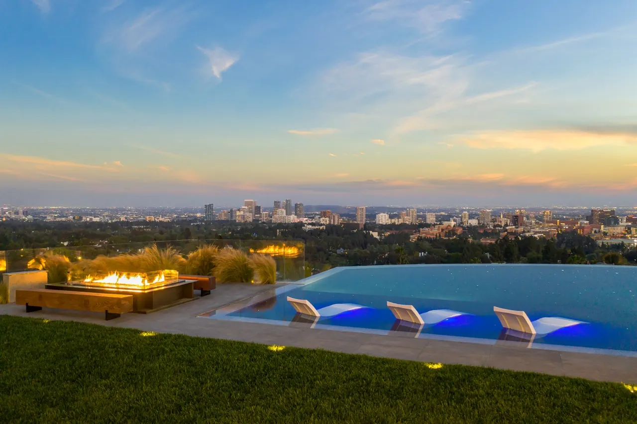 An infinity pool and fire lounge on the lawn at sunset, with the Los Angeles skyline beyond