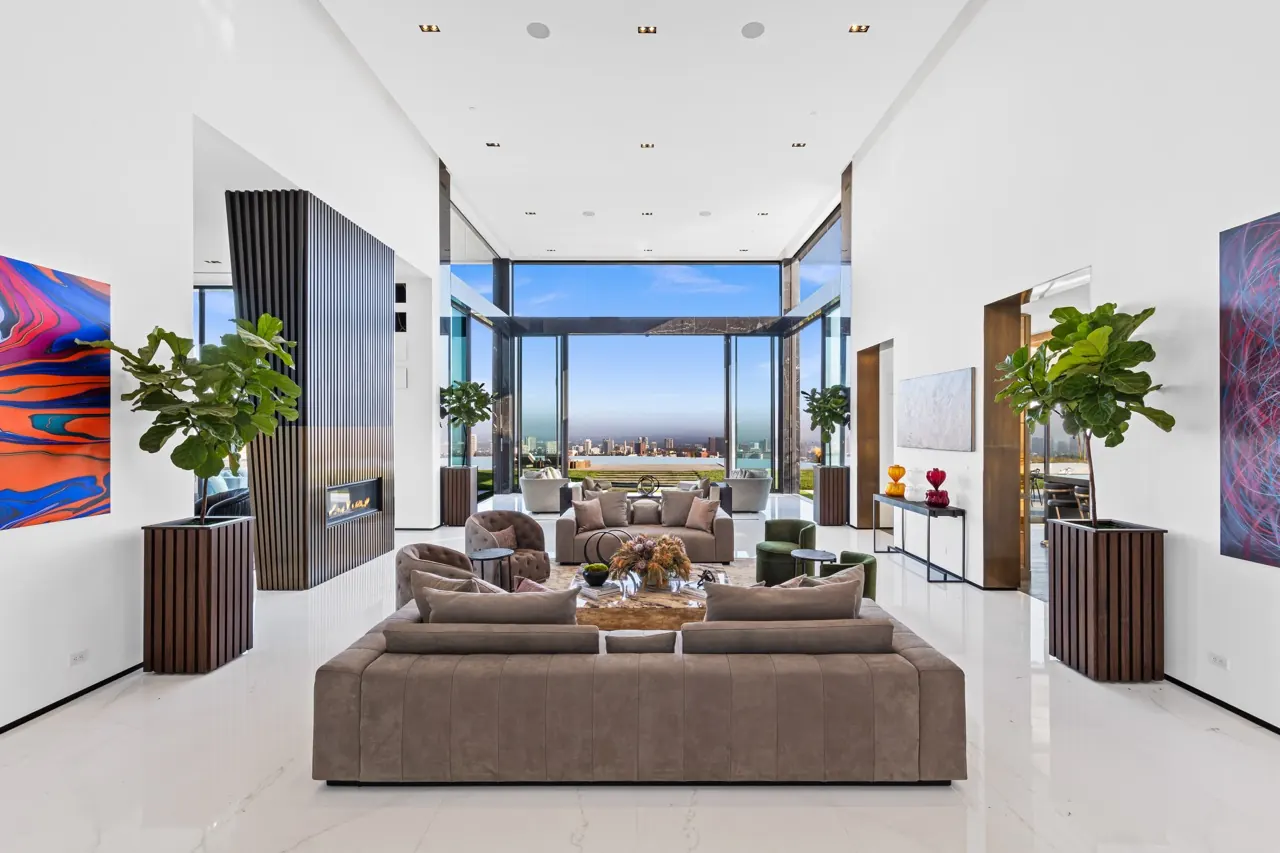 The living room: sofas on a white stone floor between a fireplace column and large artworks, opening to the view