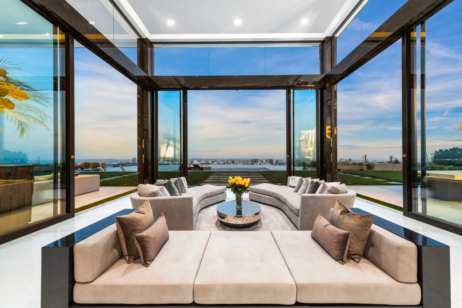 A glass lounge pavilion with a built-in sofa, framed in dark steel, looking over the city
