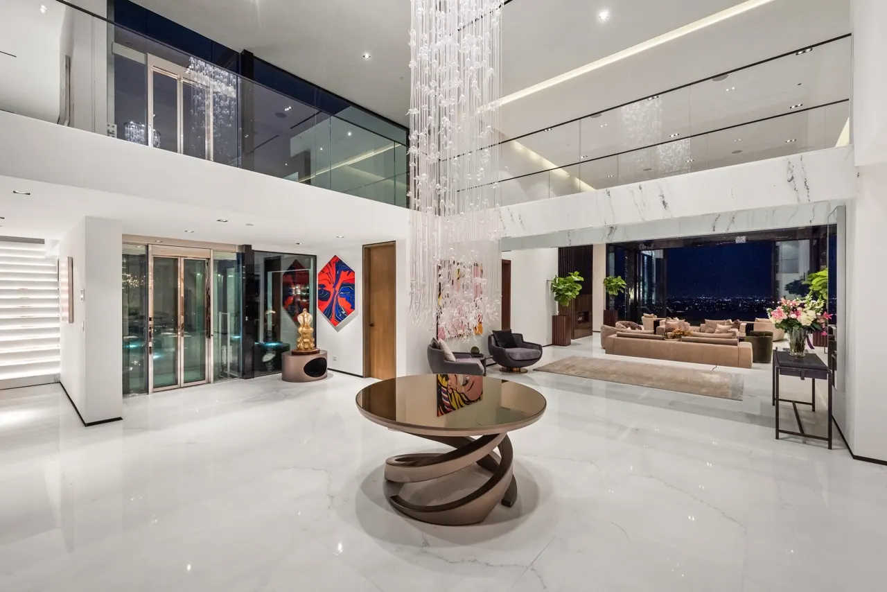 A double-height gallery with a sculptural bronze table beneath a hanging crystal installation