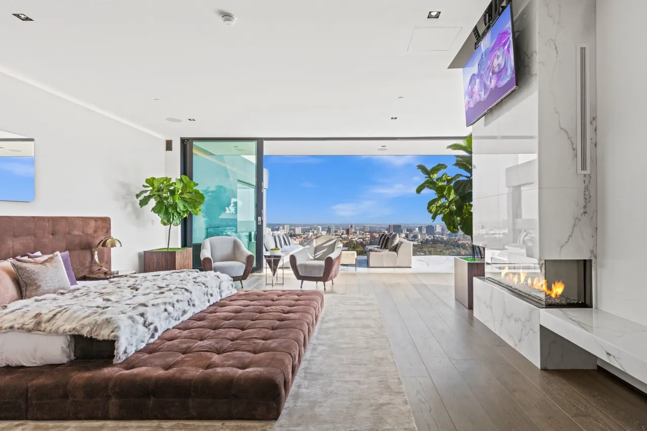 The primary bedroom with a fireplace set in a marble wall and glass doors open to the city view