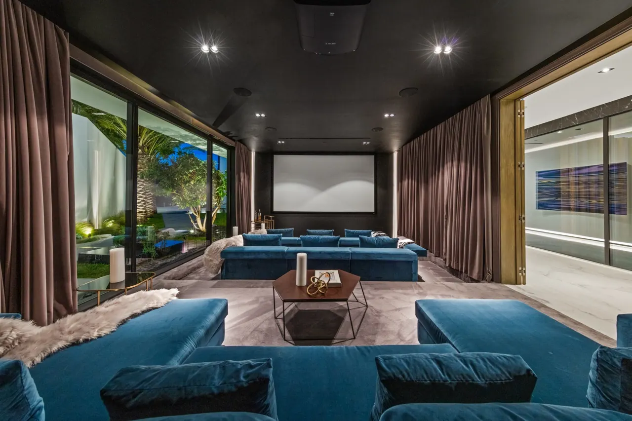 A private cinema with teal velvet sofas, a dark ceiling and curtained glass walls to the garden